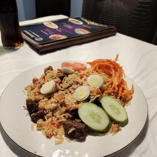 Rice dish served with meat, egg slices, carrots and cucumber at a restaurant table