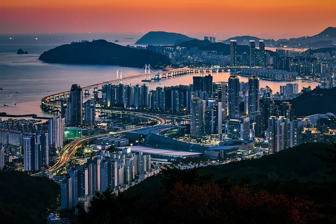 Gwangan Bridge and the illuminated towers of Gwangalli Beach under a warm sunset-to-night sky