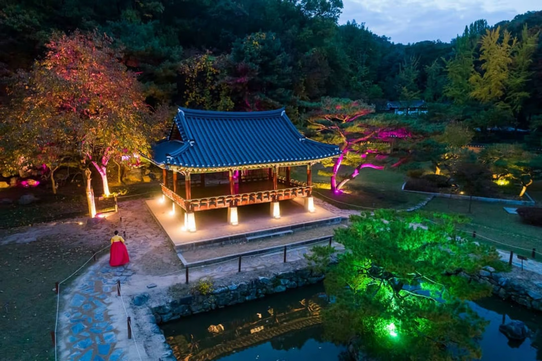 Hanok pavilion lit by colourful night festival lighting with a guest in hanbok walking past