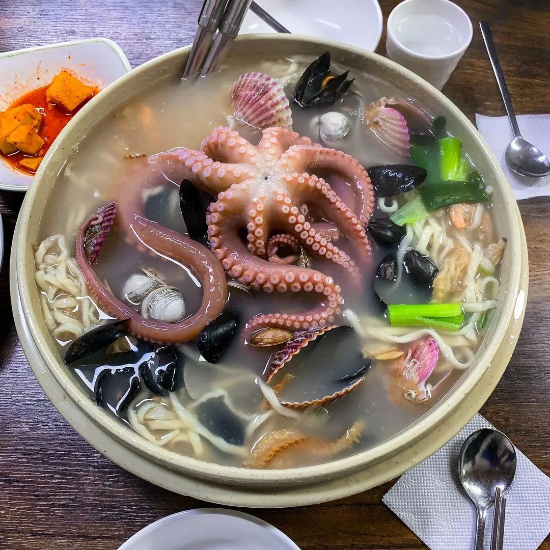 Large bowl of seafood kalguksu noodles topped with octopus, mussels and scallops