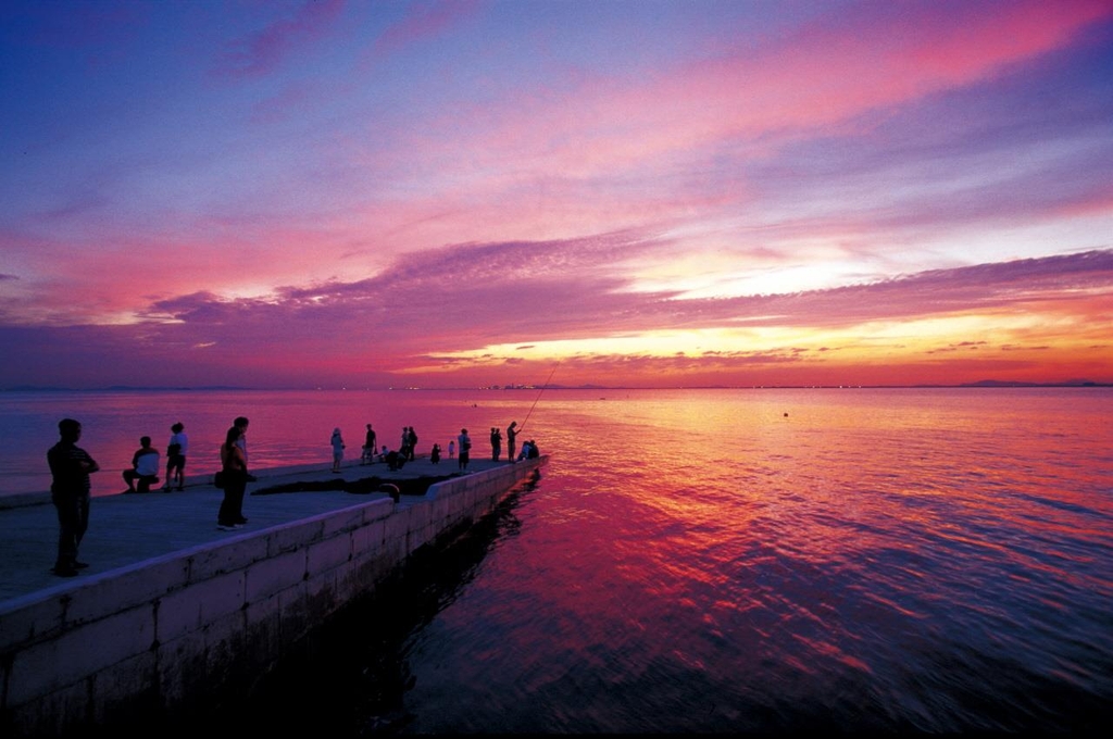 People watching a vivid pink and orange sunset over the Yellow Sea from Oido