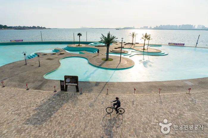 Turquoise waterfront terrace beside the calm Yellow Sea with a cyclist crossing the promenade