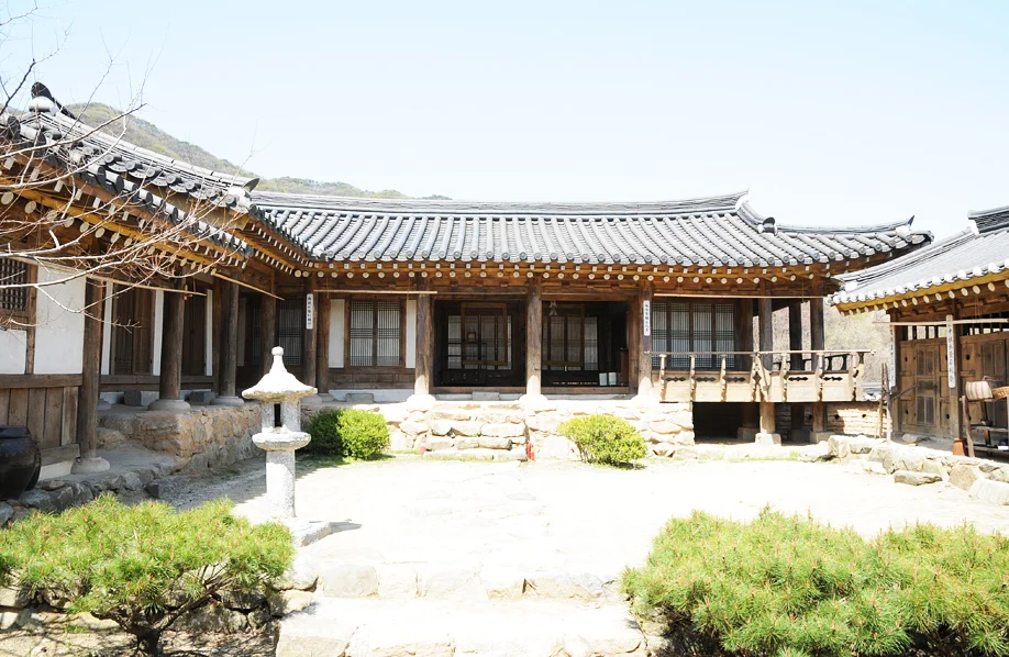 Traditional tiled-roof hanok courtyard with a stone lantern and pine shrubs at MBC Dae Jang Geum Park