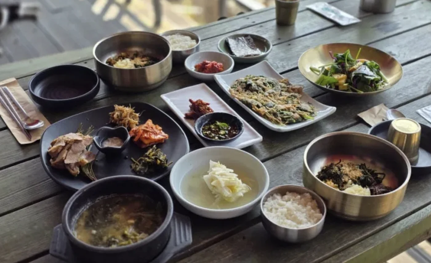 Korean set meal with rice, soup, greens, a pancake and sliced meat on a wooden table