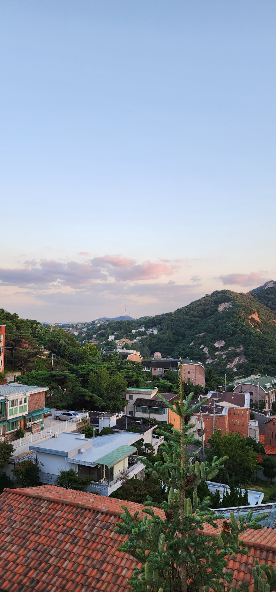 Bukchon rooftops and green slopes of Inwangsan beneath a pastel evening sky in Seoul