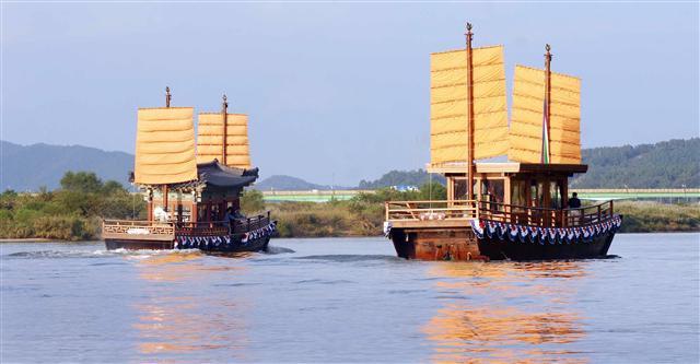 Two golden-sailed traditional Baekje boats sailing side by side on a calm river
