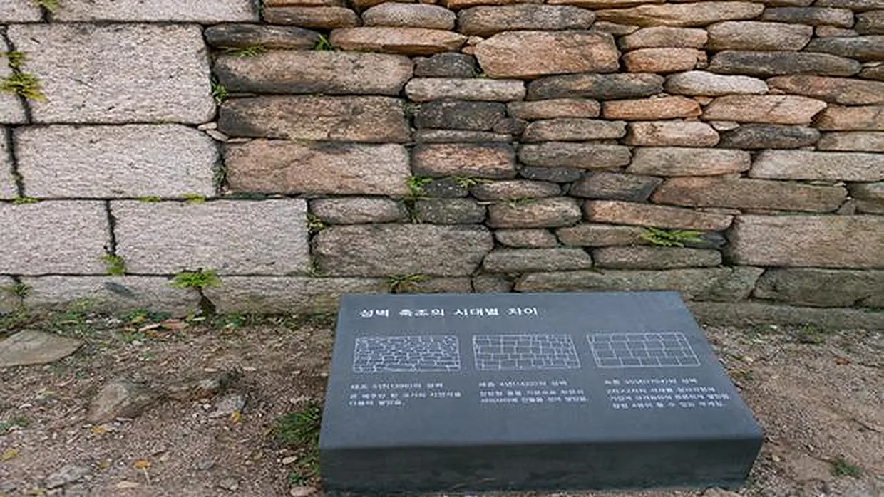Seoul City Wall stonework showing construction styles from the Taejo (1396), Sejong (1422) and Sukjong (1704) periods beside an explanatory sign