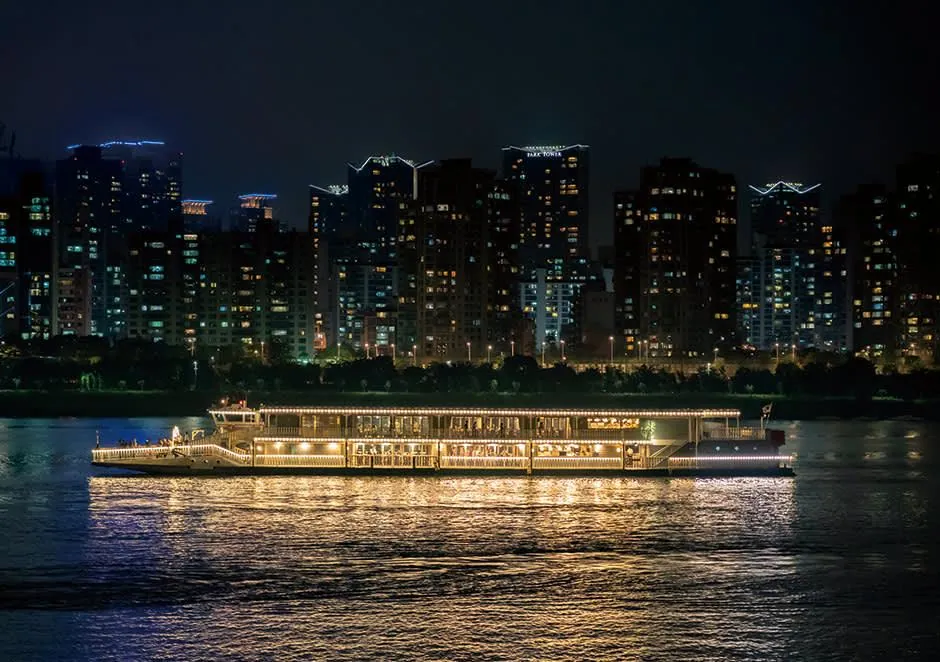 Elegant illuminated cruise boat sailing past Seoul apartment towers at night