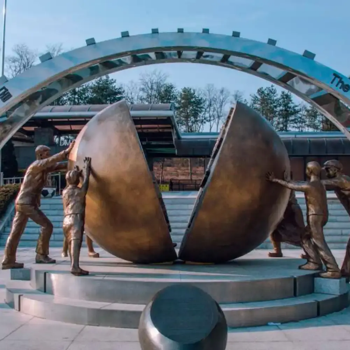 Bronze figures pushing together a split globe sculpture at the DMZ peace park