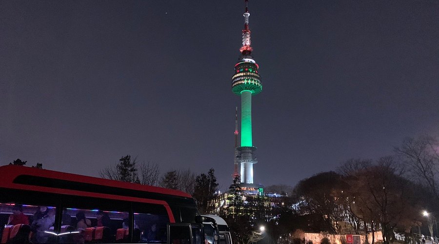 N Seoul Tower illuminated at night above tour buses on Namsan