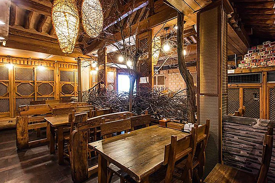 Warmly lit interior of a traditional Korean restaurant with wooden tables and hanok-style roof beams