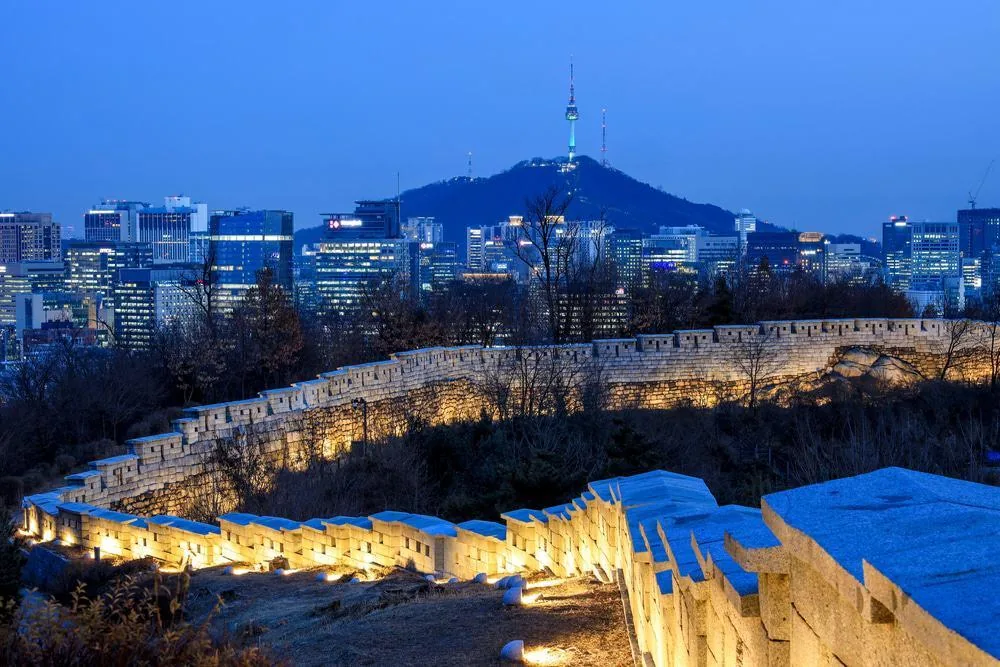 Seoul City Wall glowing under warm ground lights at dusk with N Seoul Tower above the city skyline