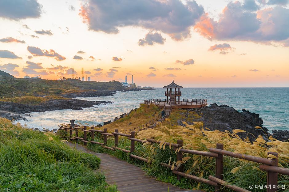Wooden coastal pavilion on Jeju at sunset surrounded by silver grass and the sea