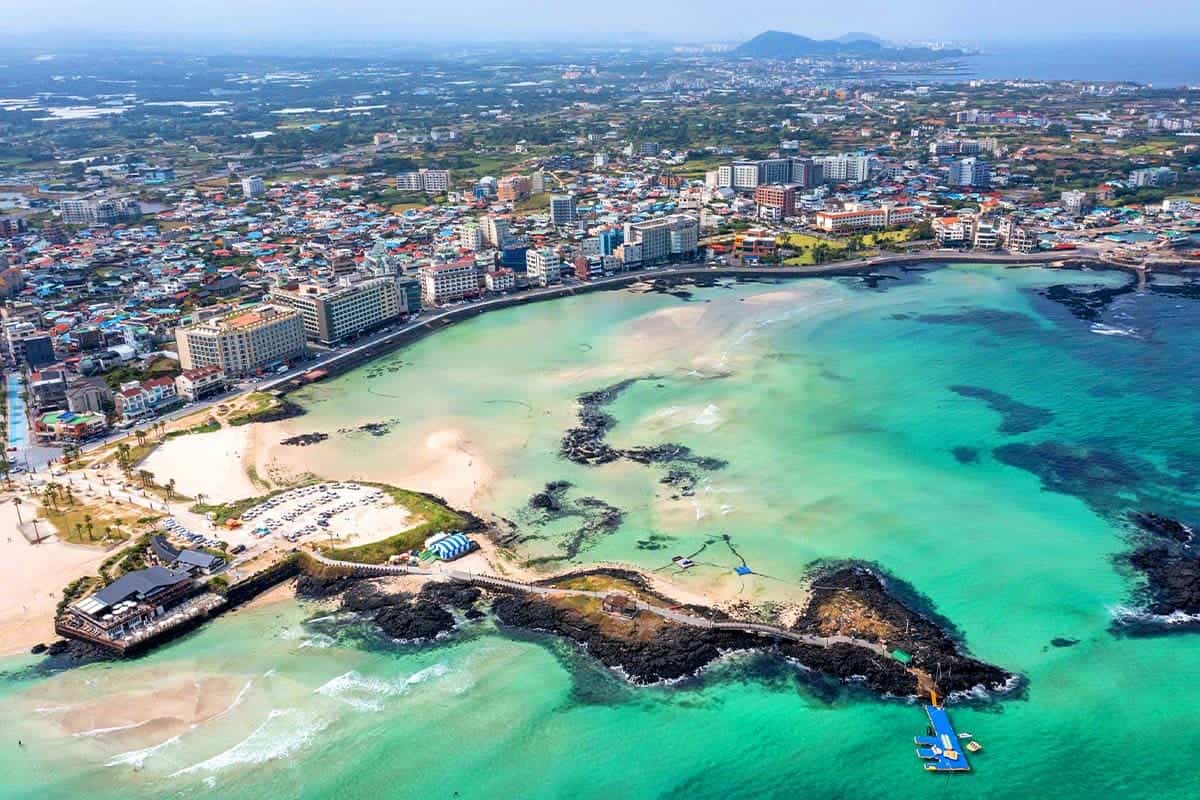 Aerial view of Woljeongri beach on Jeju with turquoise water, white sand and a black volcanic headland