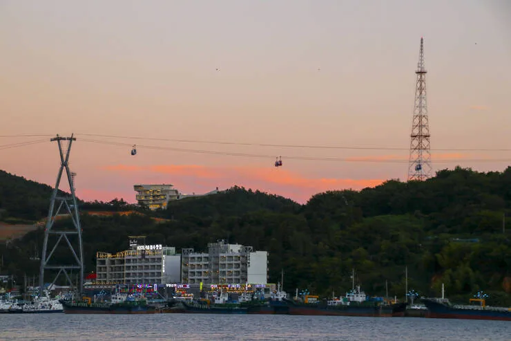 Evening light over Yeosu's harbour coast with cable car towers, moored ships and waterfront buildings