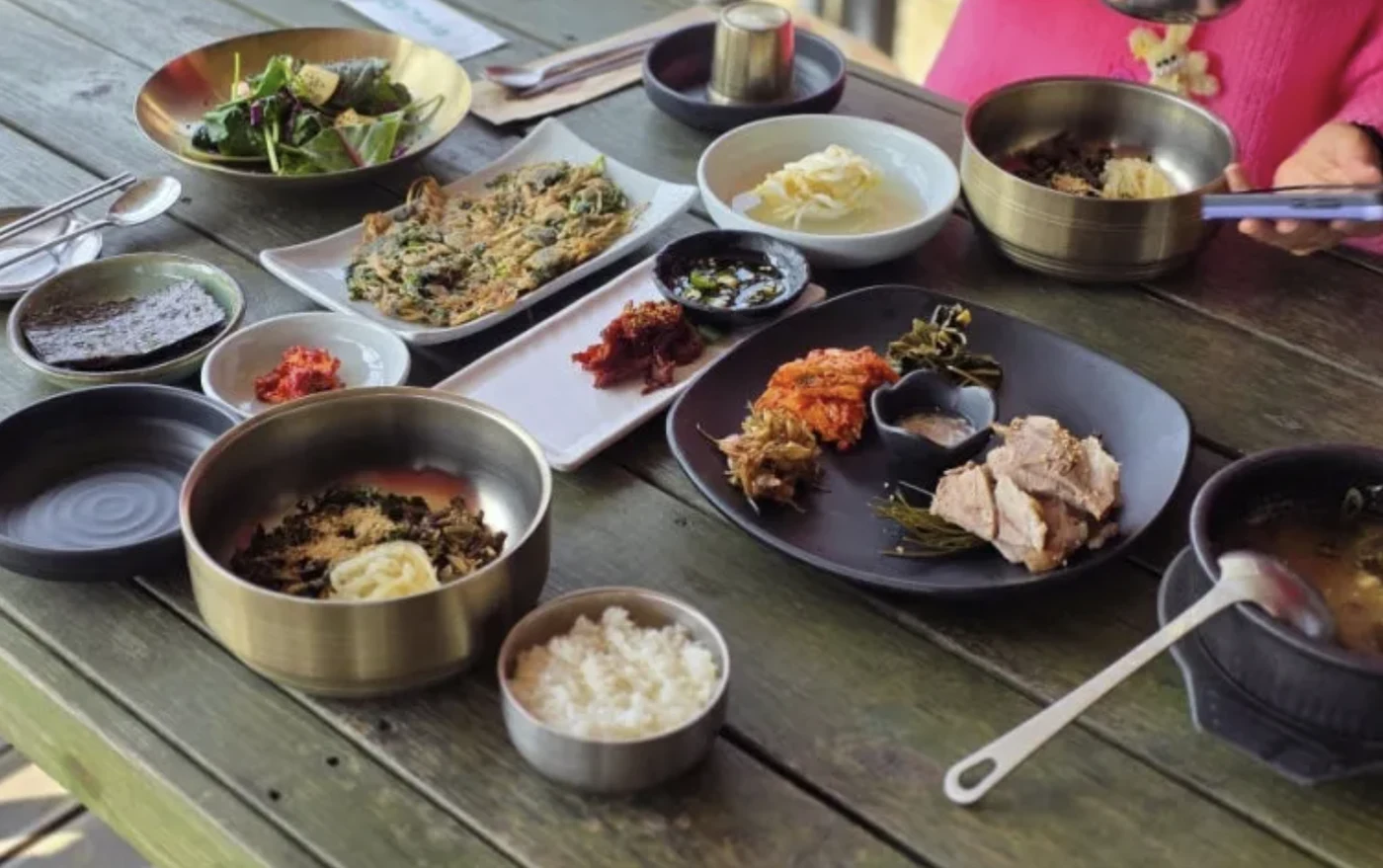 Guests sharing a Korean meal with metal rice bowls, side dishes, soup and a savoury pancake