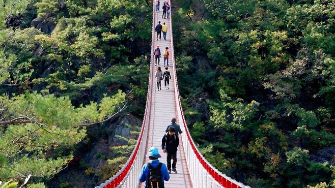 Hikers crossing the red Gamaksan suspension bridge above a wooded valley