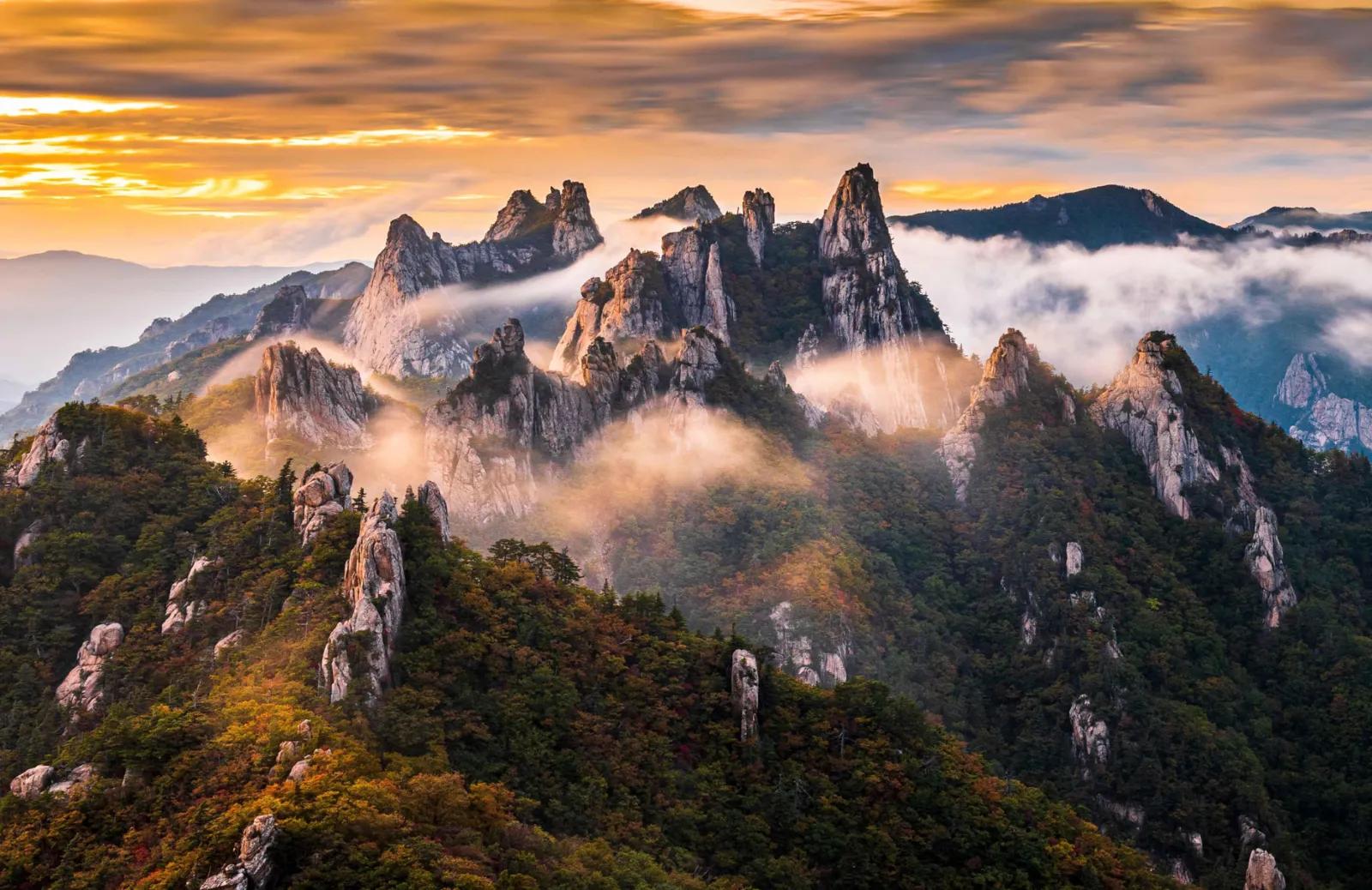 Golden sunrise over Seoraksan's granite peaks and autumn forest seen from Gwittaegicheongbong, with morning mist in the valleys