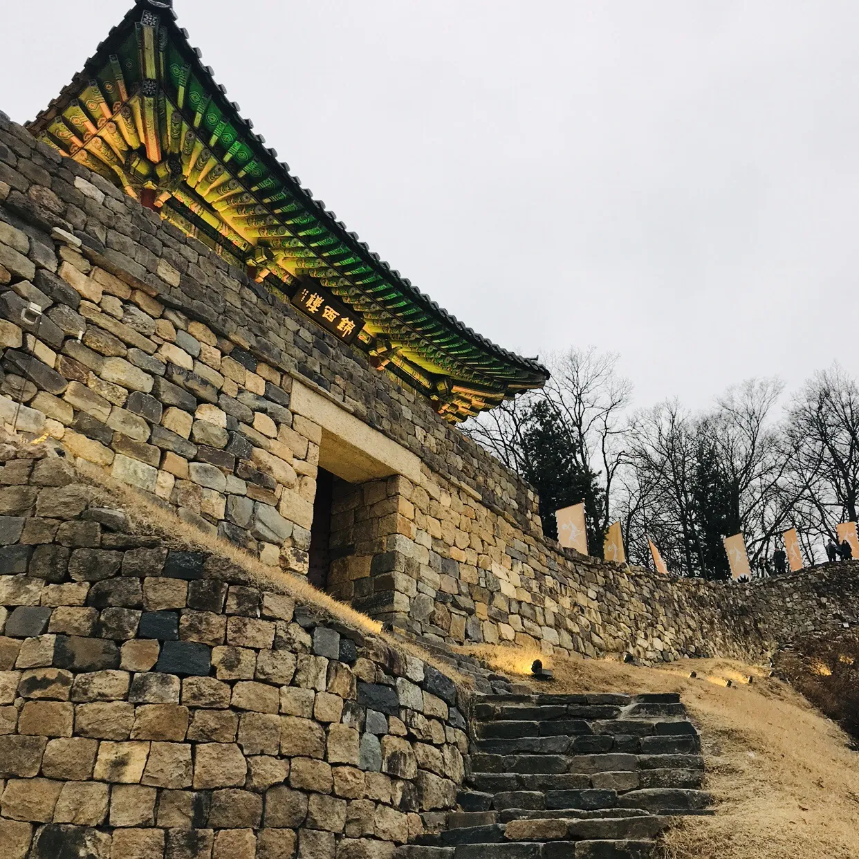 Traditional gate rising above the illuminated stone walls of Gongsanseong Fortress in Gongju