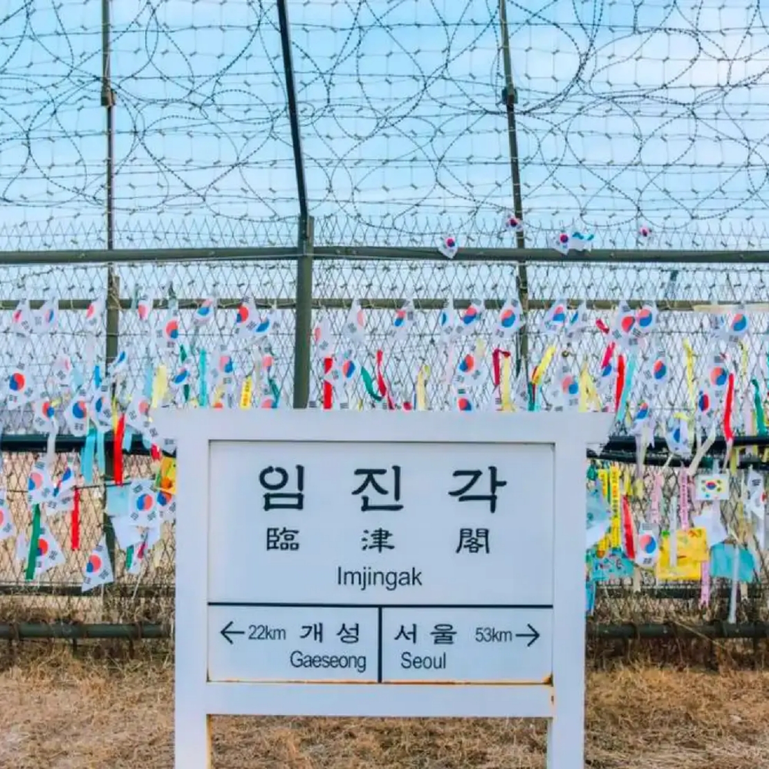 Imjingak signpost in front of a barbed-wire fence covered in ribbons and Korean flags