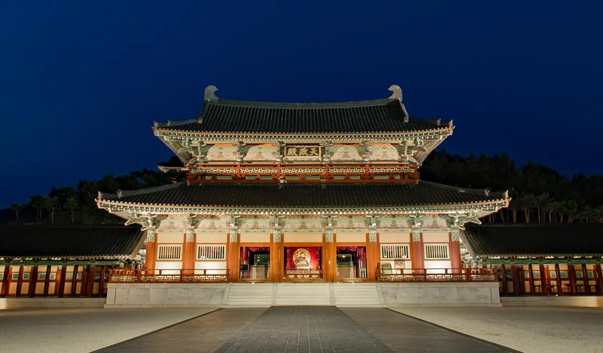 Illuminated Baekje royal palace hall glowing against a deep blue night sky