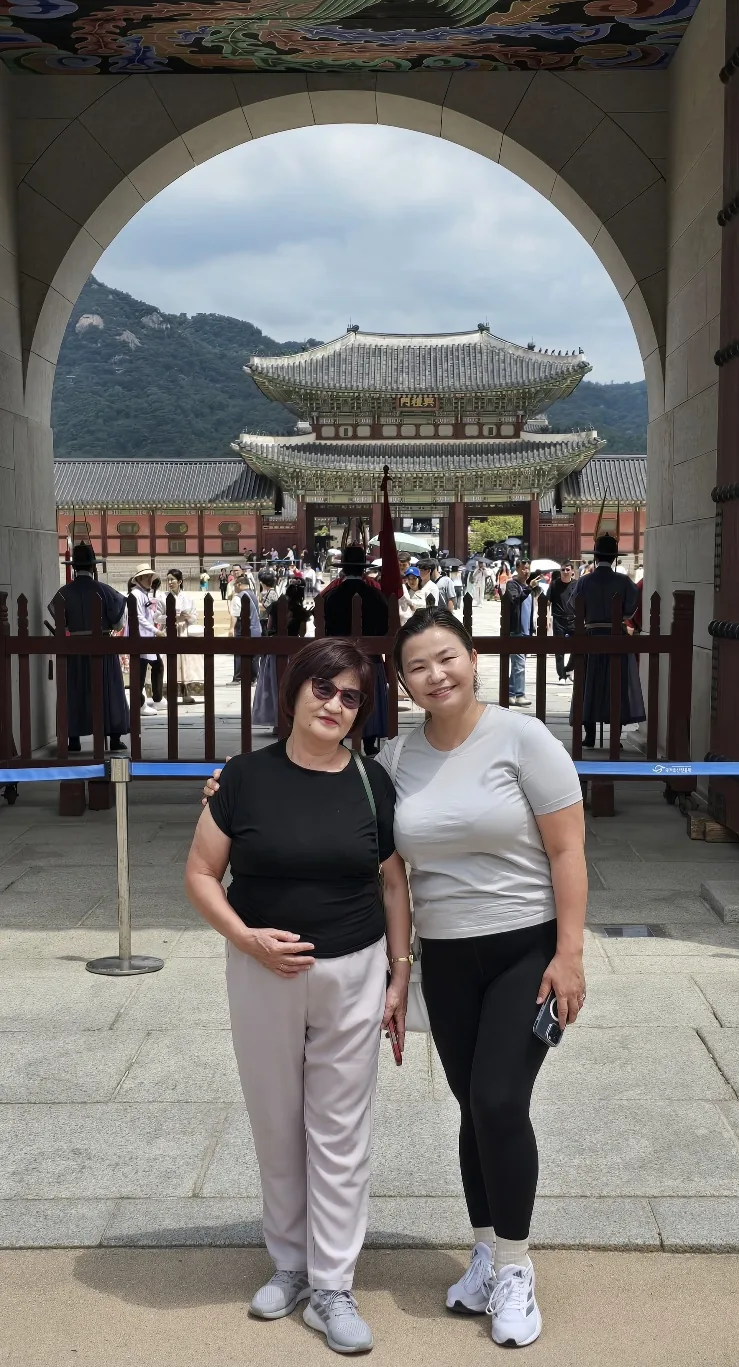 Two travelers beneath a decorated palace gateway with a traditional pavilion and mountain in the background