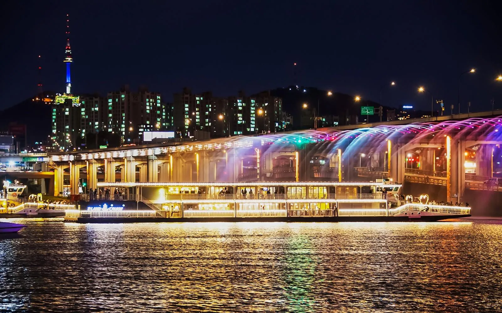 Illuminated cruise boat passing Banpo Bridge and its rainbow fountain on the Han River