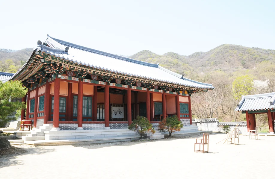 Red-pillared traditional hall with mountains behind at MBC Dae Jang Geum Park