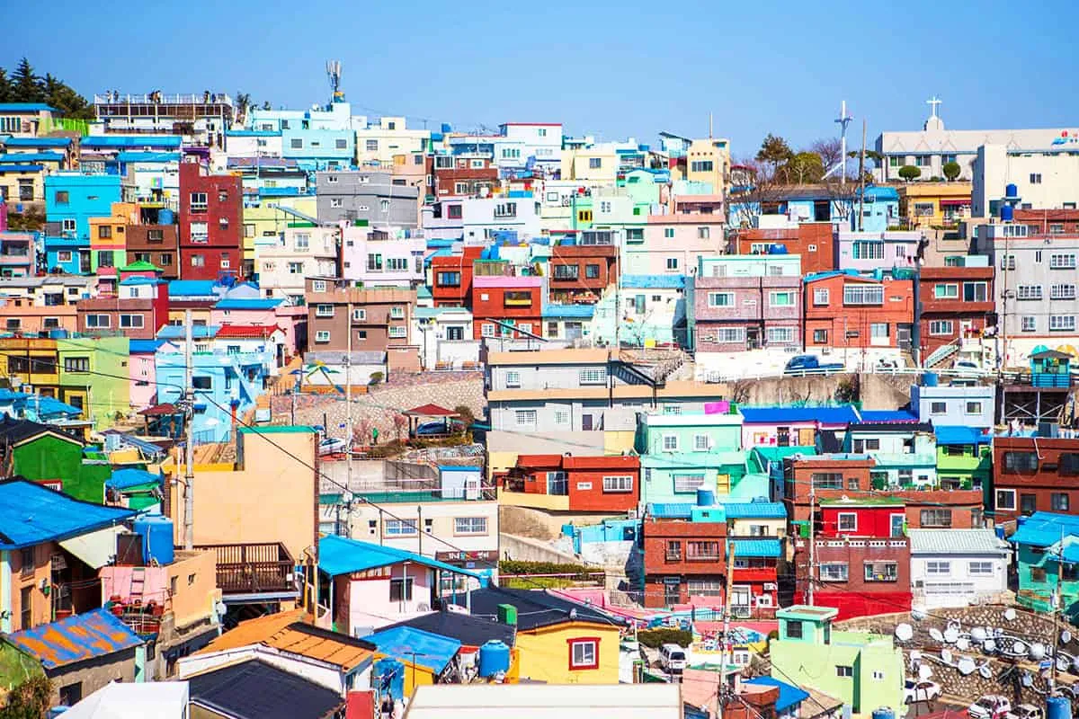 Colourful pastel houses stacked across the hillside of Gamcheon Culture Village under a blue sky