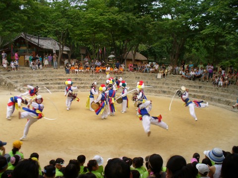 Traditional pungmul performers in colourful costumes play drums and spin ribbons in an outdoor arena at Korean Folk Village in Yongin