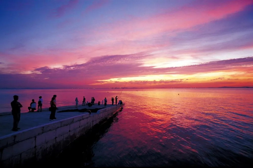 People watching a vivid pink and orange sunset over the Yellow Sea from Oido