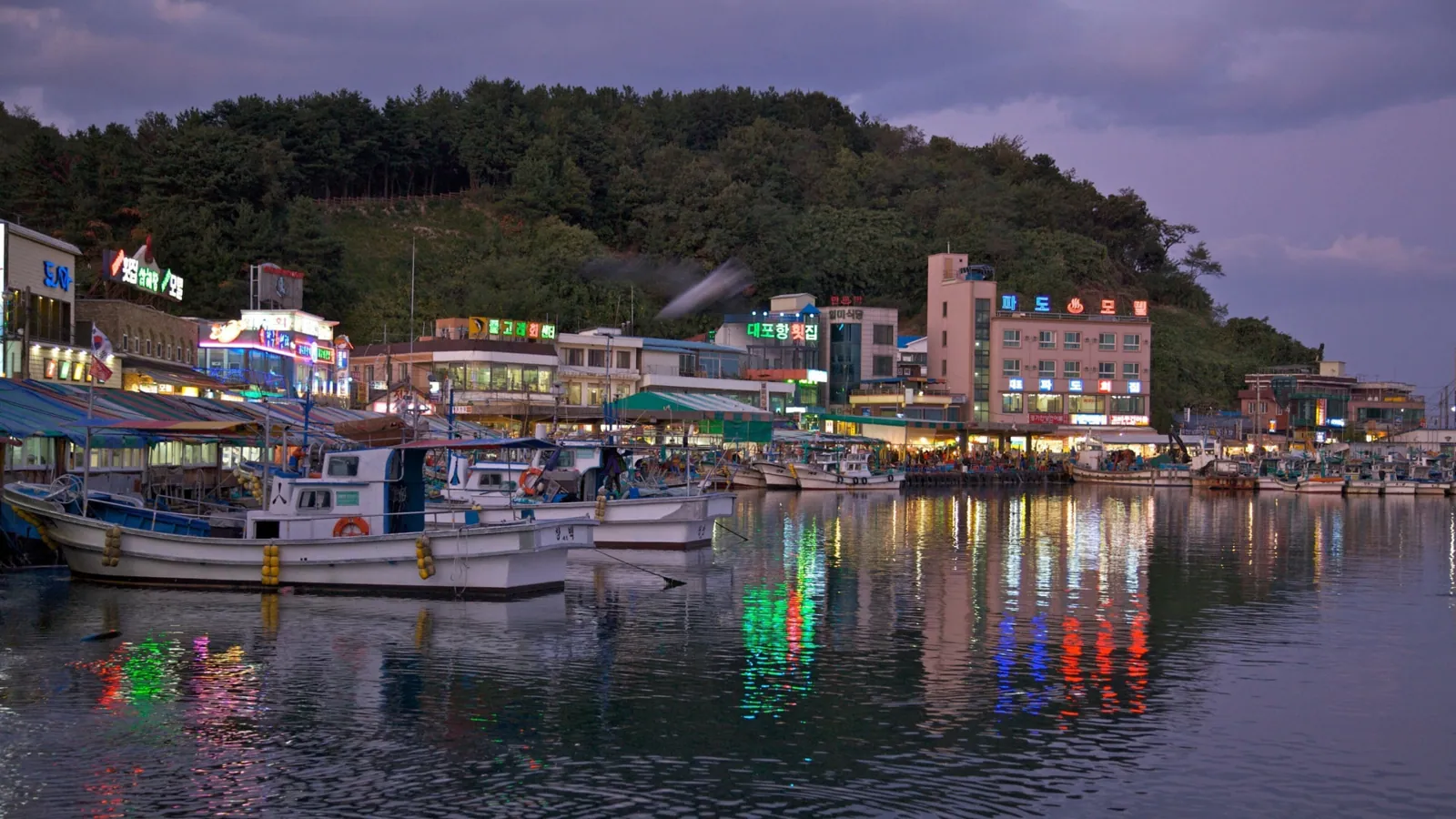 Fishing boats and colourful restaurant lights reflecting on Daepohang harbour at dusk