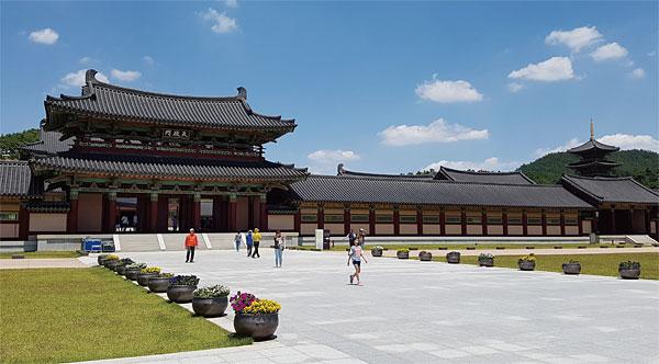 Visitors crossing the wide stone plaza of Baekje Cultural Land under a blue summer sky