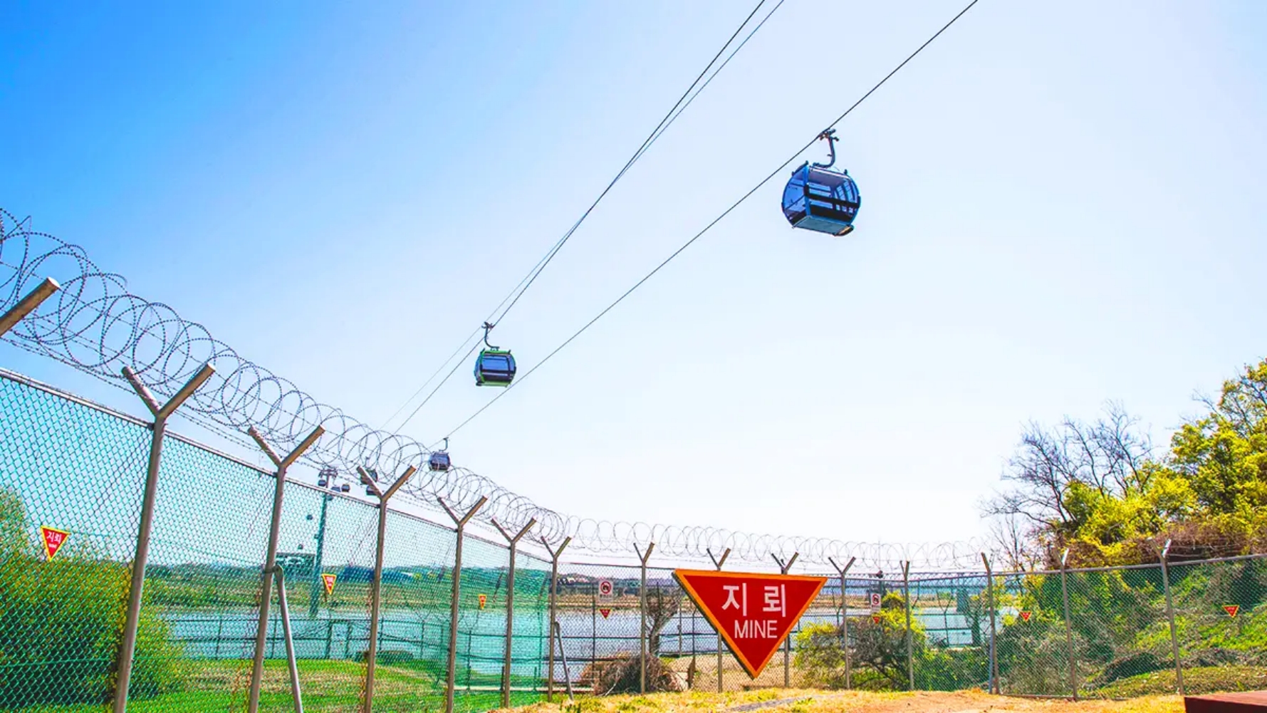 Cabinas del teleférico de la DMZ en Paju cruzando sobre una zona vallada con advertencia de minas