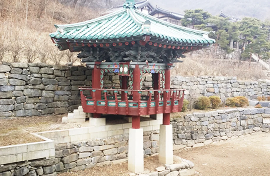 Painted red and green bell pavilion beside stone walls at MBC Dae Jang Geum Park