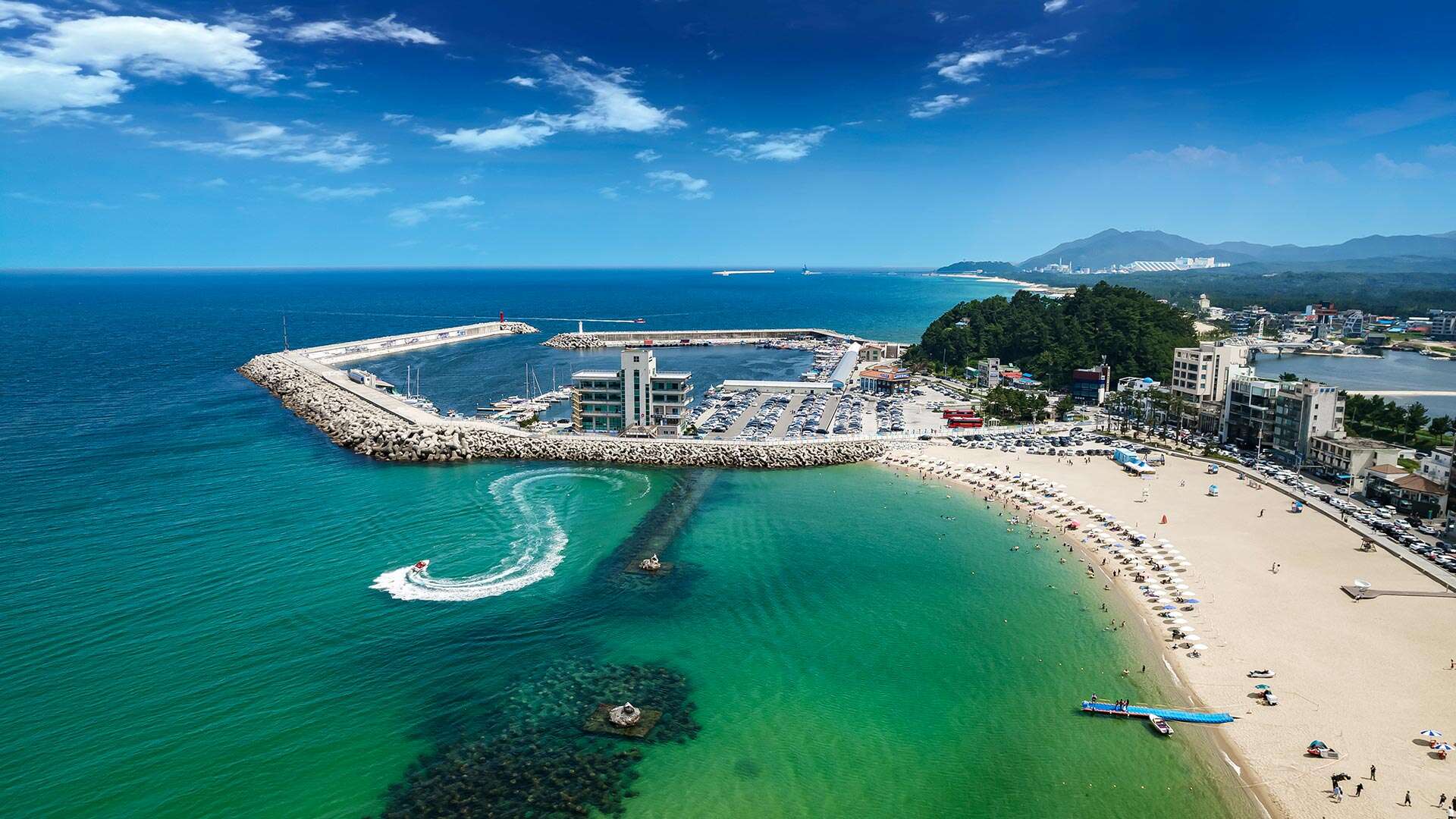 Aerial view of Sokcho's white sand beach, turquoise water and marina breakwater on a clear summer day