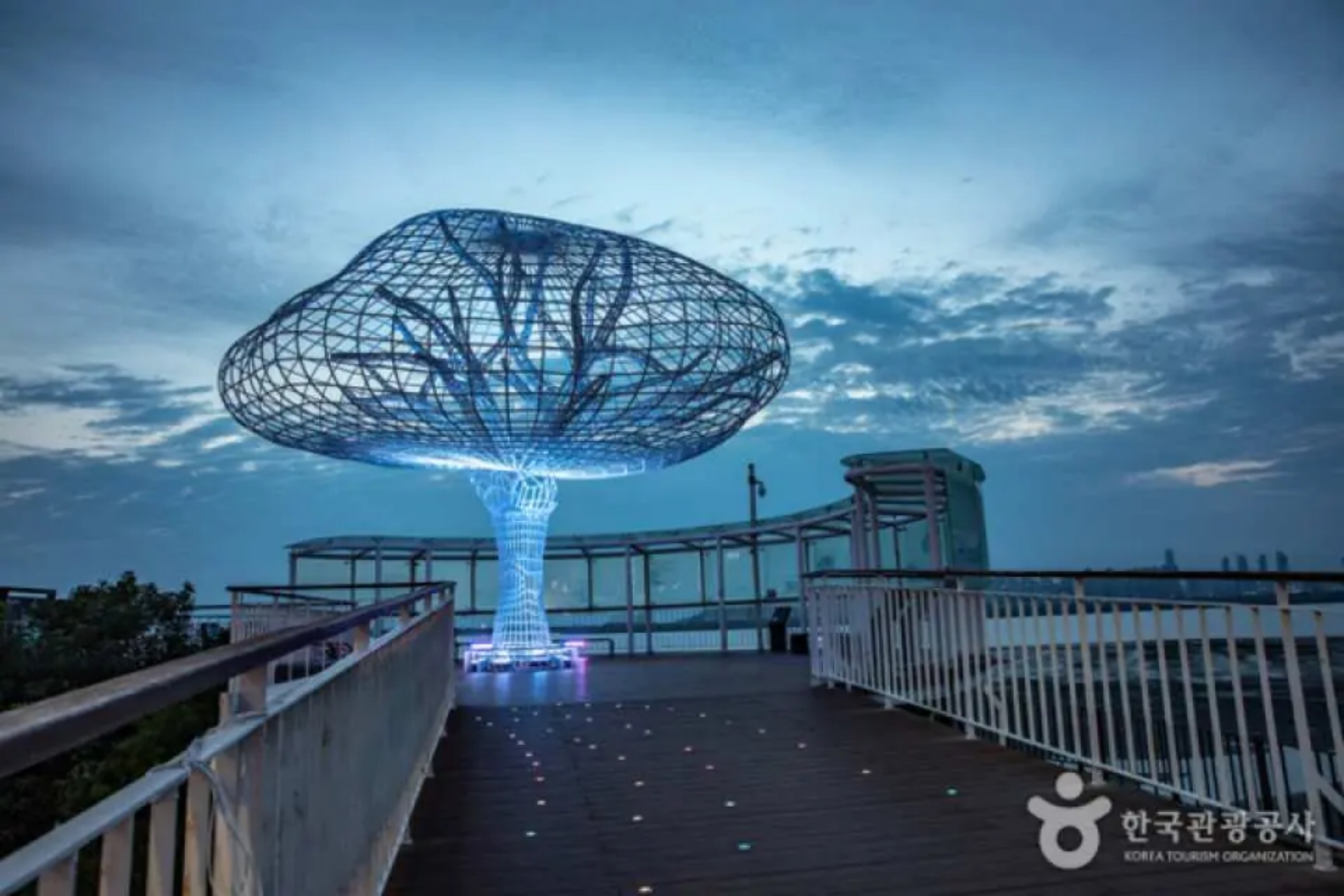 Illuminated Tree of Life sculpture on Oido's coastal boardwalk at blue hour
