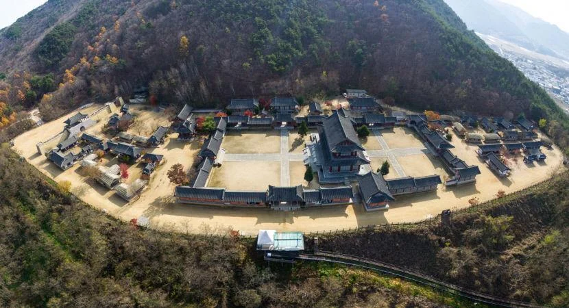 Aerial view of traditional buildings and courtyards at Mungyeongsaejae Open Set below a wooded mountain