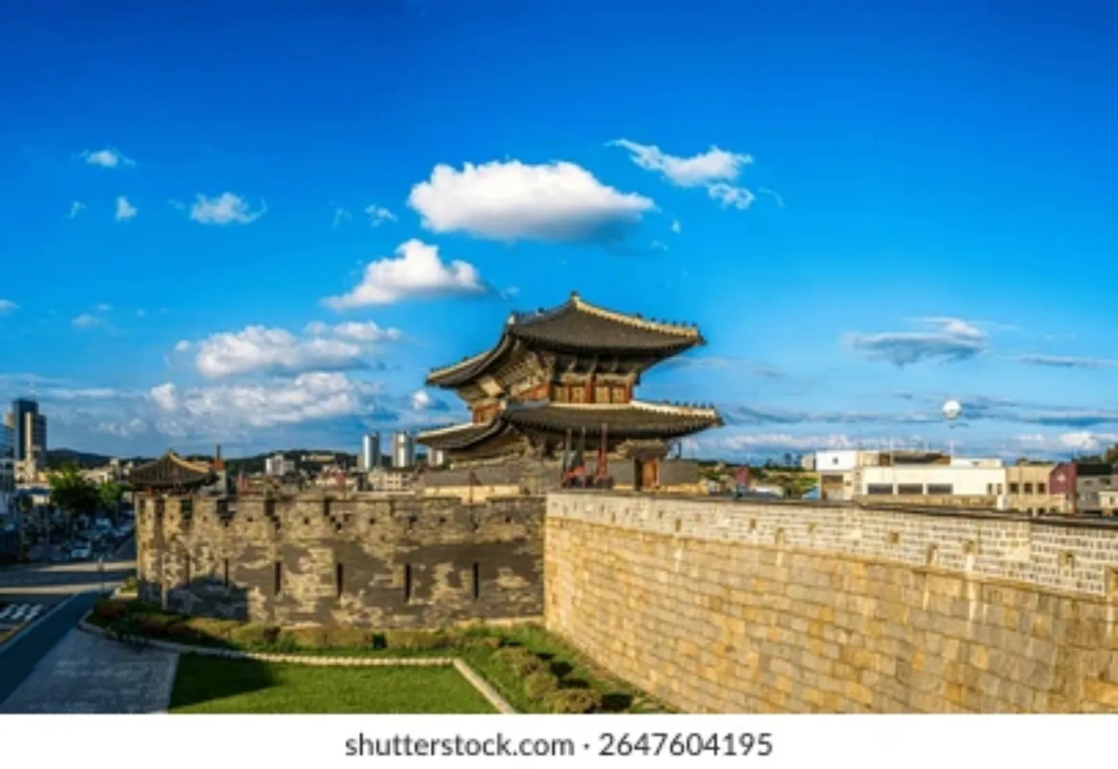 Hwaseong Fortress gate and stone wall under a bright blue sky in Suwon