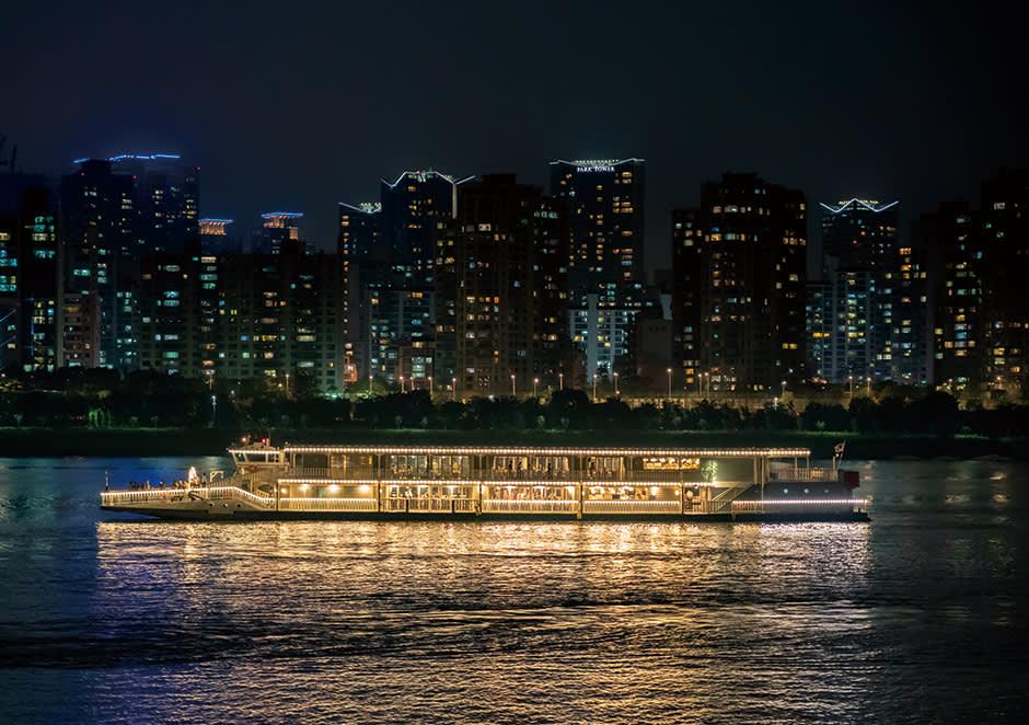 Elegant illuminated cruise boat sailing past Seoul apartment towers at night