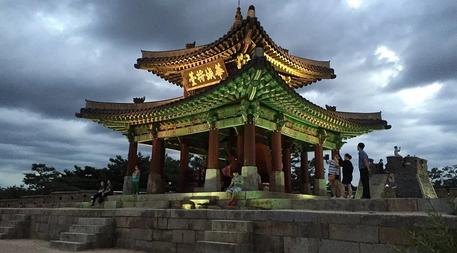 Illuminated Hwaseong Fortress pavilion at dusk with visitors on the stone steps