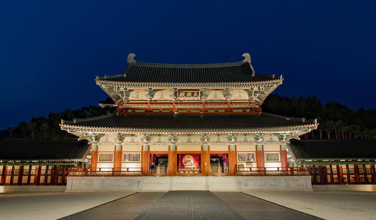 Illuminated Baekje royal palace hall glowing against a deep blue night sky
