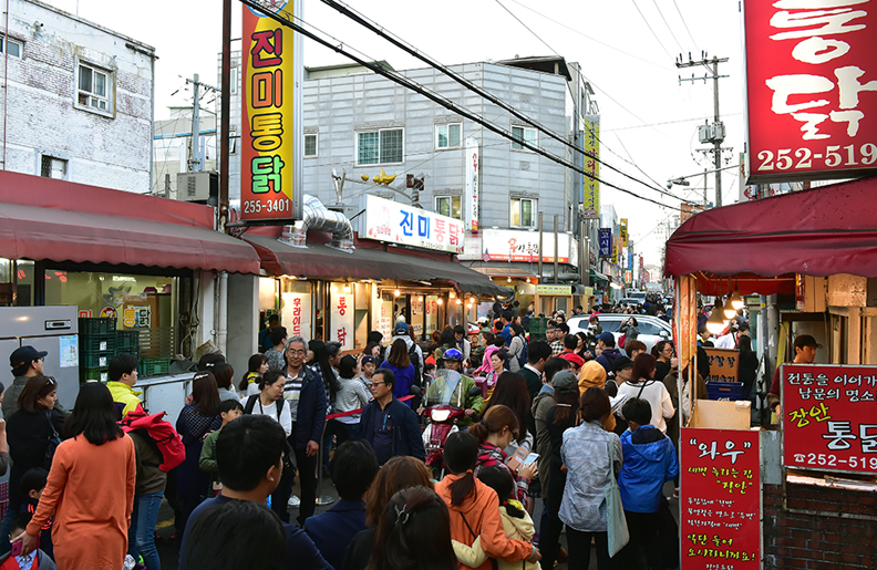 Crowded Tongdak Geori fried chicken street with neon signs in the evening