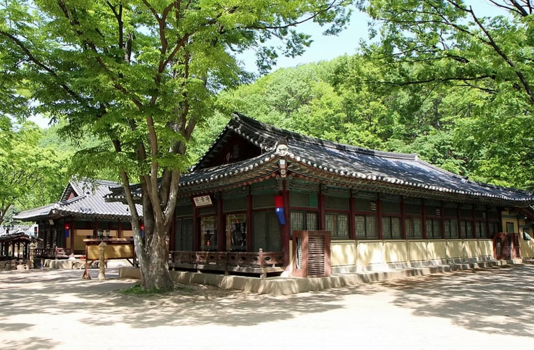 Long tiled-roof magistrate's office building beneath green summer trees at the folk village