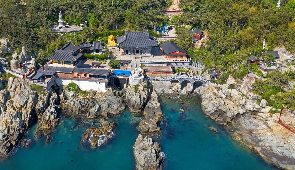 Aerial view of Haedong Yonggungsa Temple above clear blue water and rocky coastline in Busan