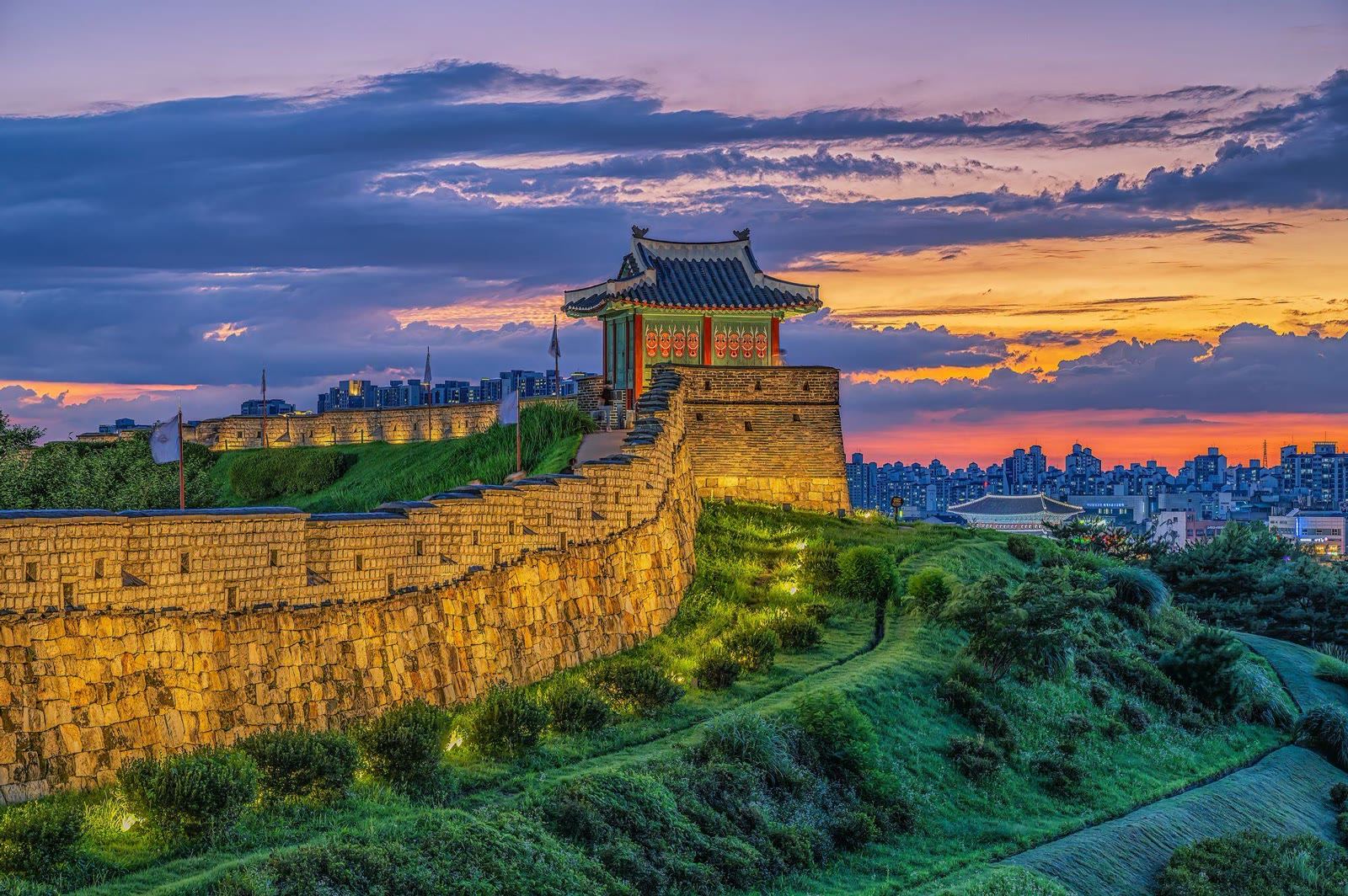 Hwaseong Fortress walls and pavilion lit at dusk above the Suwon skyline