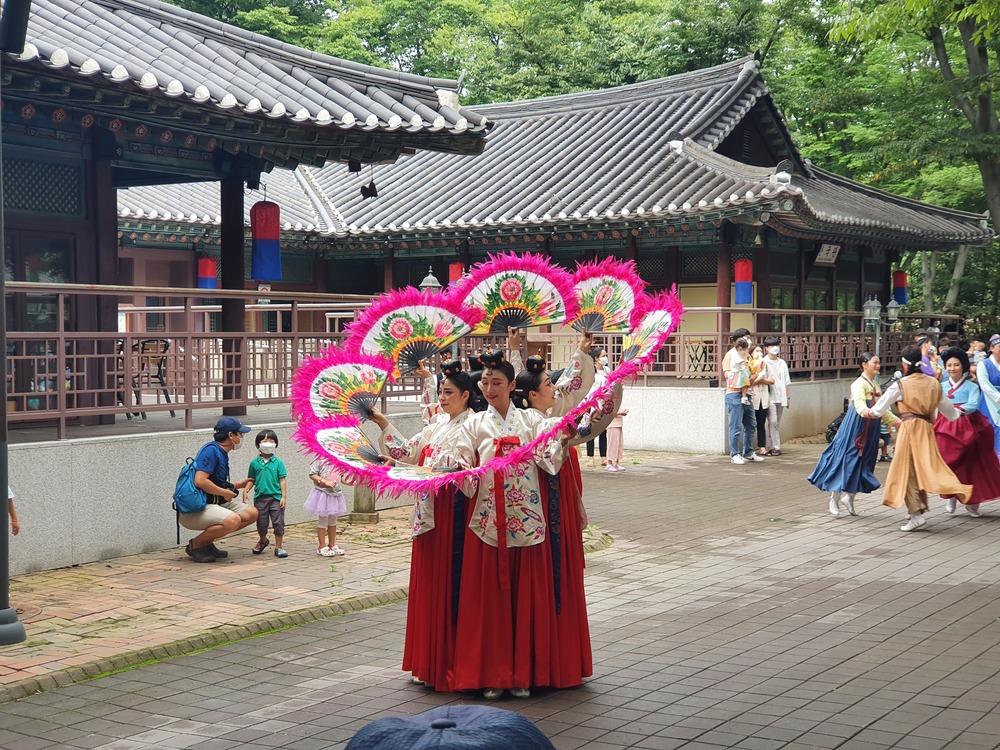 Performers in red hanbok opening pink fans in a fan dance at the Korean Folk Village