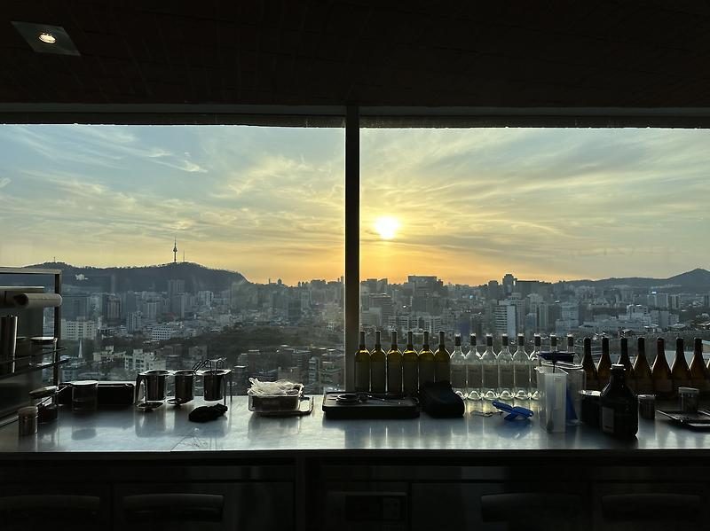 Café lounge counter silhouetted against a golden sunset over the Seoul skyline and N Seoul Tower