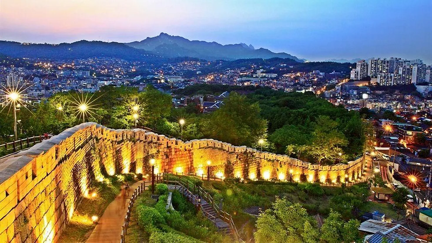 Illuminated Seoul City Wall at Naksan Park winding along the ridge above the glittering city lights at dusk