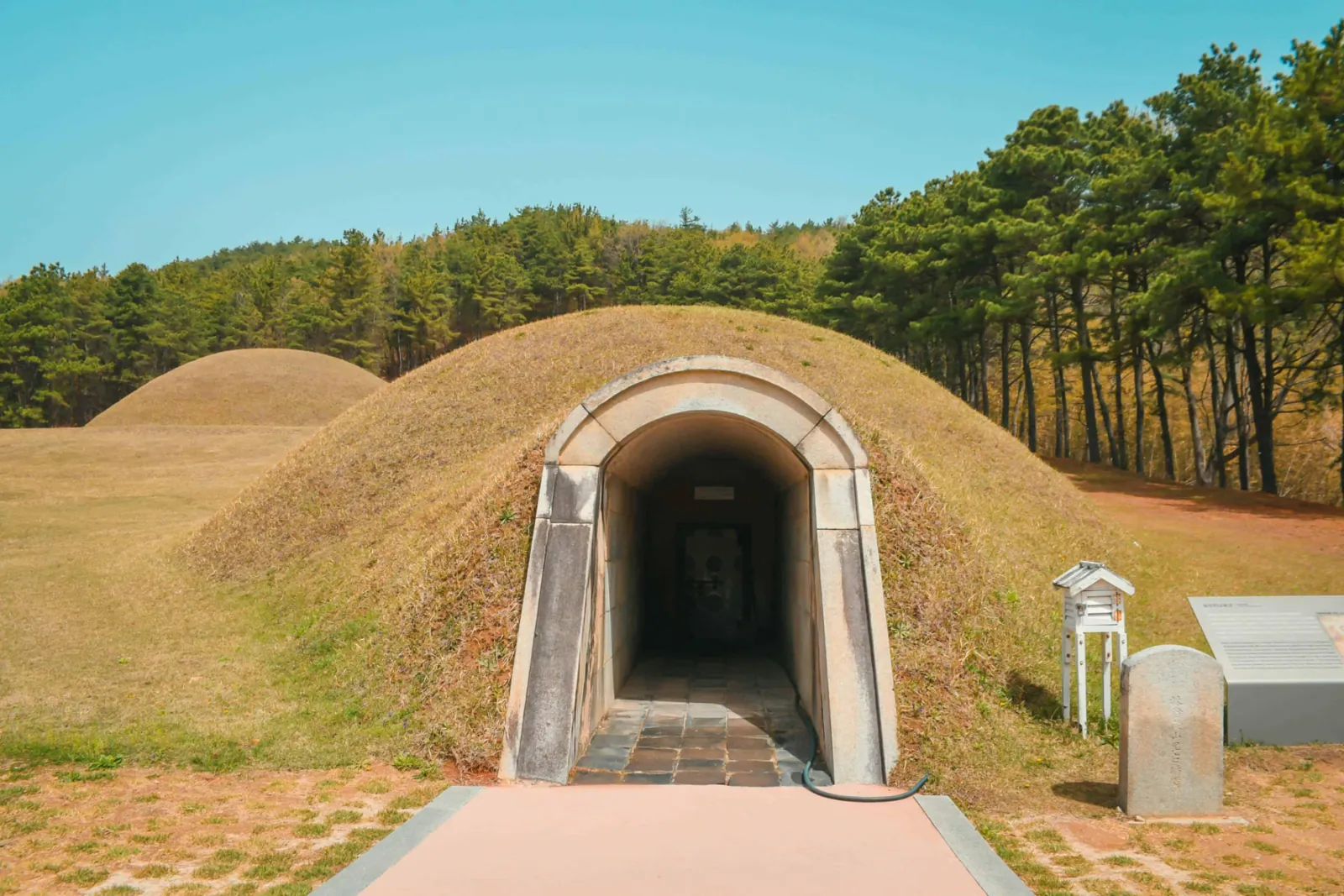 Arched stone entrance leading into a restored Baekje royal tomb in a grassy mound